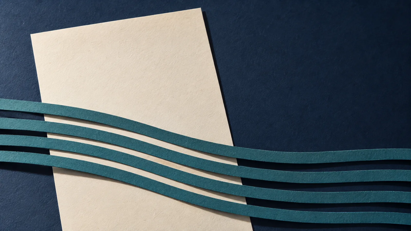 Papiercollage: ein leeres Blatt in Elfenbein liegt schraeg auf marineblauem Untergrund, vier gebogene petrolfarbene Streifen laufen ueber seine untere Haelfte hinweg und ueber den Bildrand hinaus.